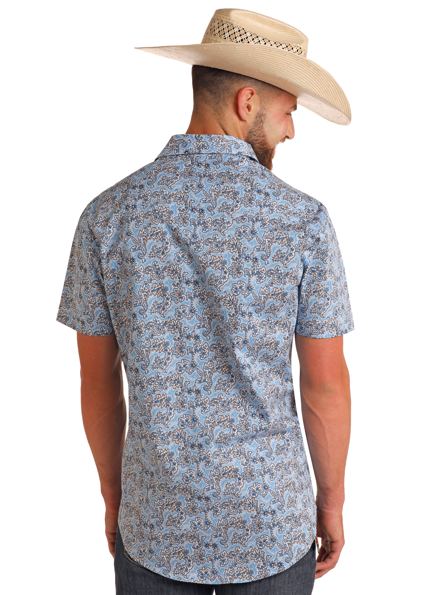 A man in a Rock & Roll Denim Slim Fit Blue Paisley Short Sleeve Snap Shirt, dark jeans, and a straw cowboy hat stands with his back to the camera.