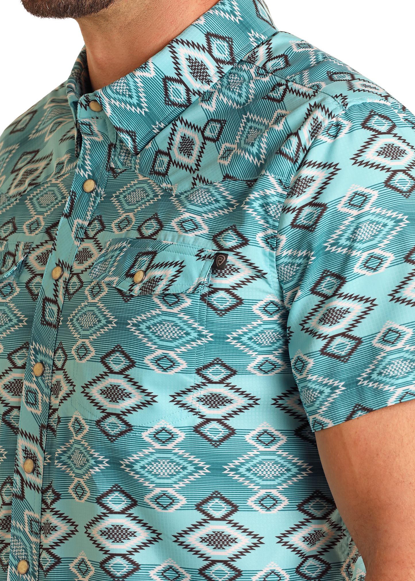 Close-up of a person in the Rock & Roll Denim TEK Western Aztec Diamond Short Sleeve Shirt, featuring a turquoise and black-and-white geometric print, front pocket, brass-tone buttons—showing only the lower face, neck, and upper arm.
