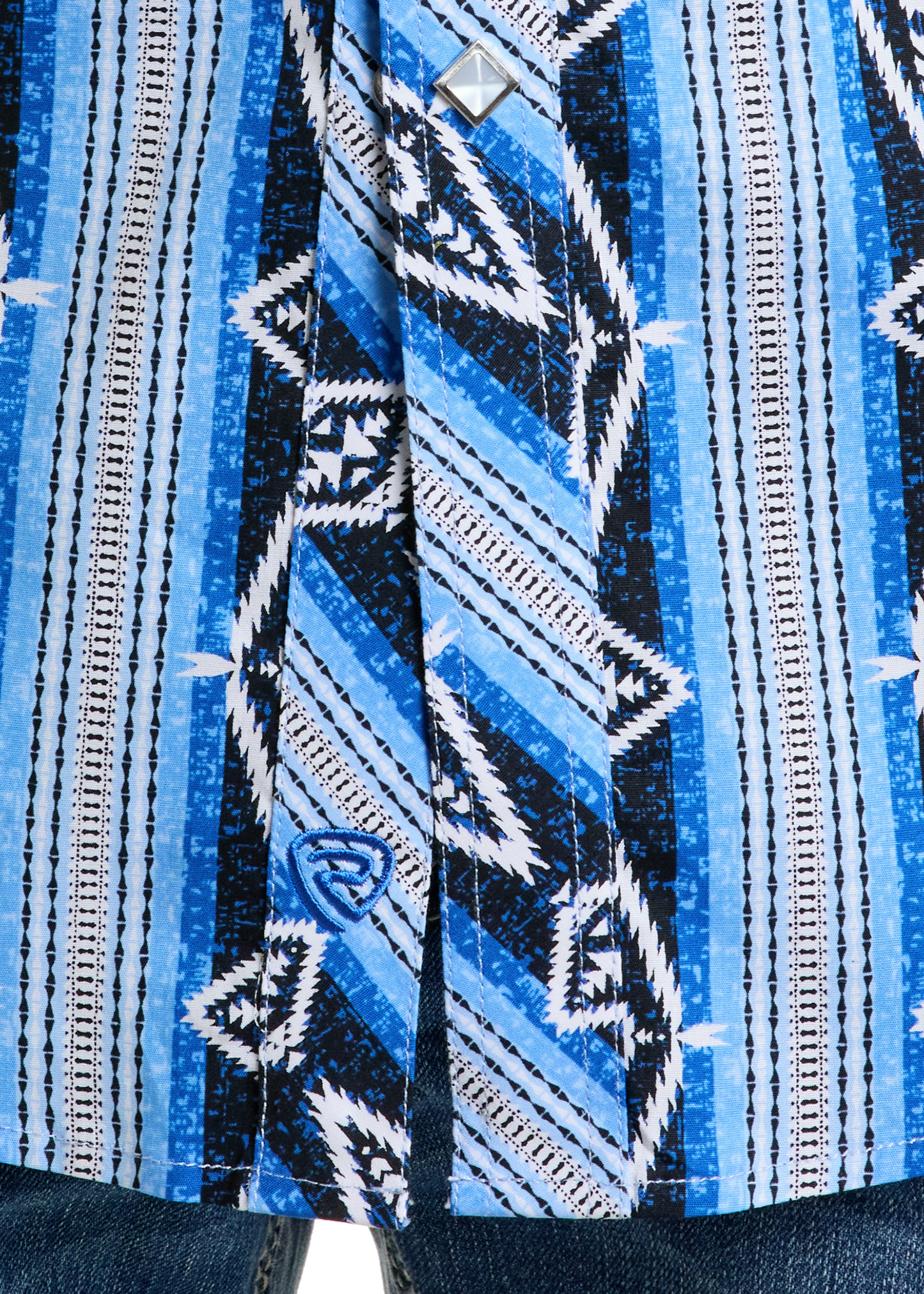 Close-up of the Rock & Roll Denim Slim Fit Vertical Aztec Short Sleeve Snap Shirt in blue, black, and white geometric patterns, buttoned and paired with blue denim jeans visible at the bottom.