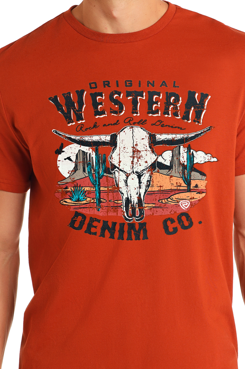 A person wears a red Rock & Roll Denim Western Denim Graphic Tee featuring a cow skull, cacti, desert scenery, and the text "Original Western Denim Co.
