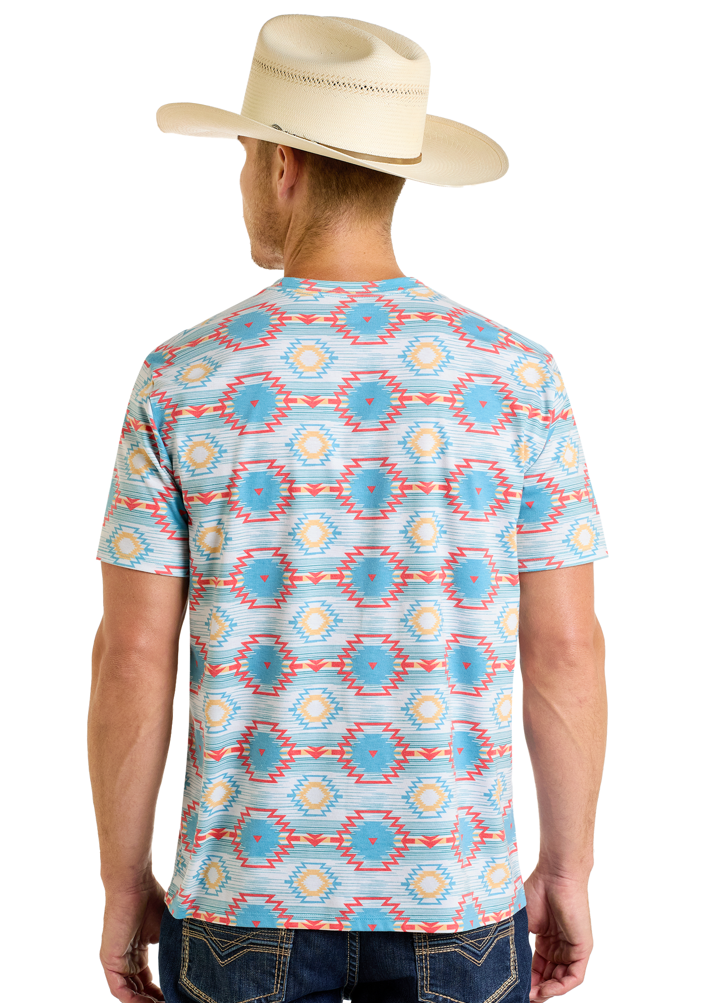 A man in a cream cowboy hat and Rock & Roll Denim’s Turquoise Aztec All Over Print Tee, featuring colorful blue, yellow, and red geometric patterns, stands with his back facing the camera.