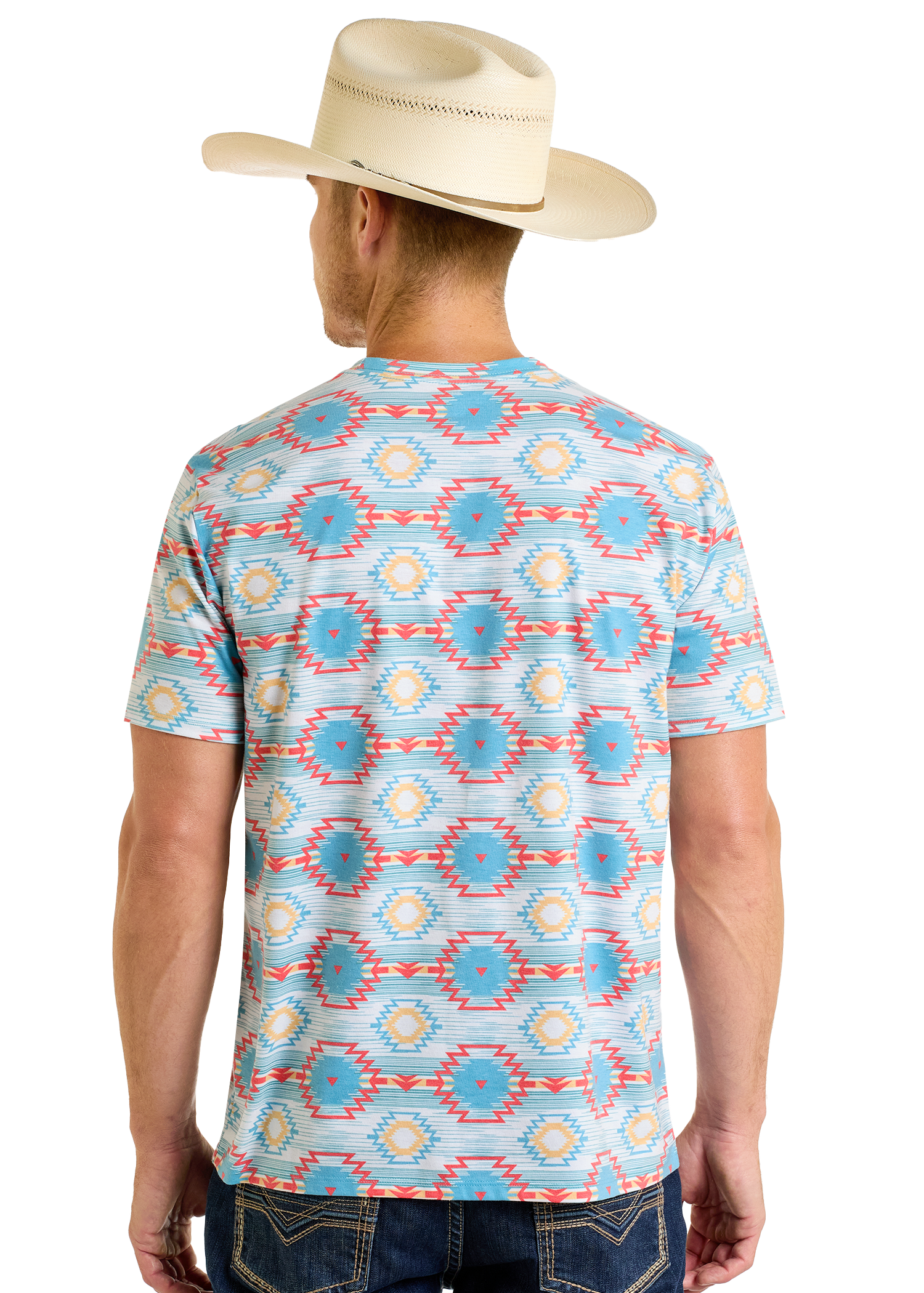 A man in a cream cowboy hat and Rock & Roll Denim’s Turquoise Aztec All Over Print Tee, featuring colorful blue, yellow, and red geometric patterns, stands with his back facing the camera.