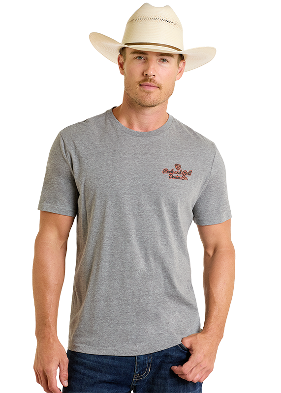 A man in a beige cowboy hat, blue jeans, and a Rock & Roll Denim “Denim Co Unisex Graphic Tee” with small red text on the left chest stands against a plain light background.