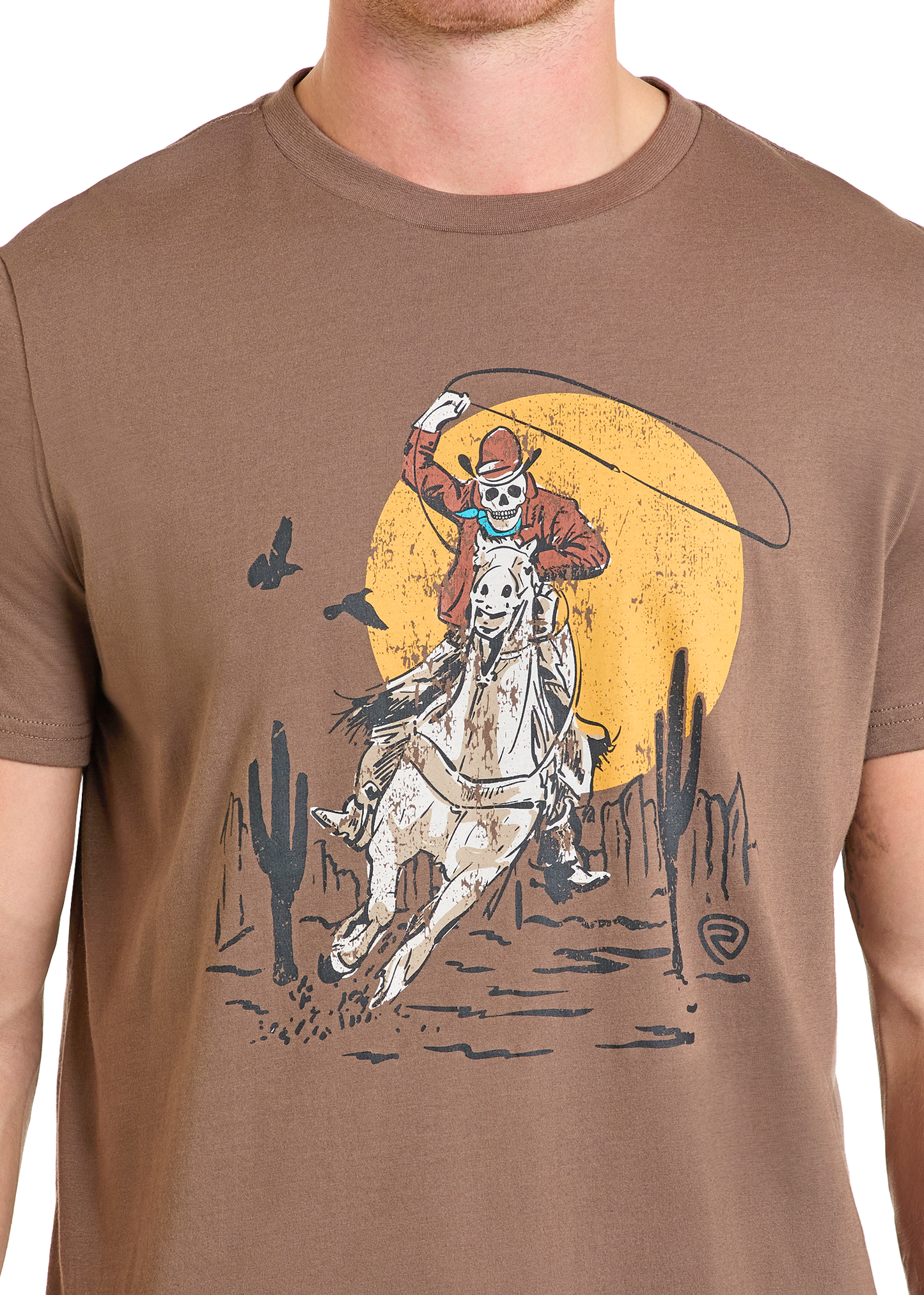 The Rock & Roll Denim Skeleton Bronco Rider Graphic Tee features a skeleton rider on a white horse with a lasso, surrounded by cacti and a yellow sun. Enjoy its comfortable fit and bold, western-inspired style.