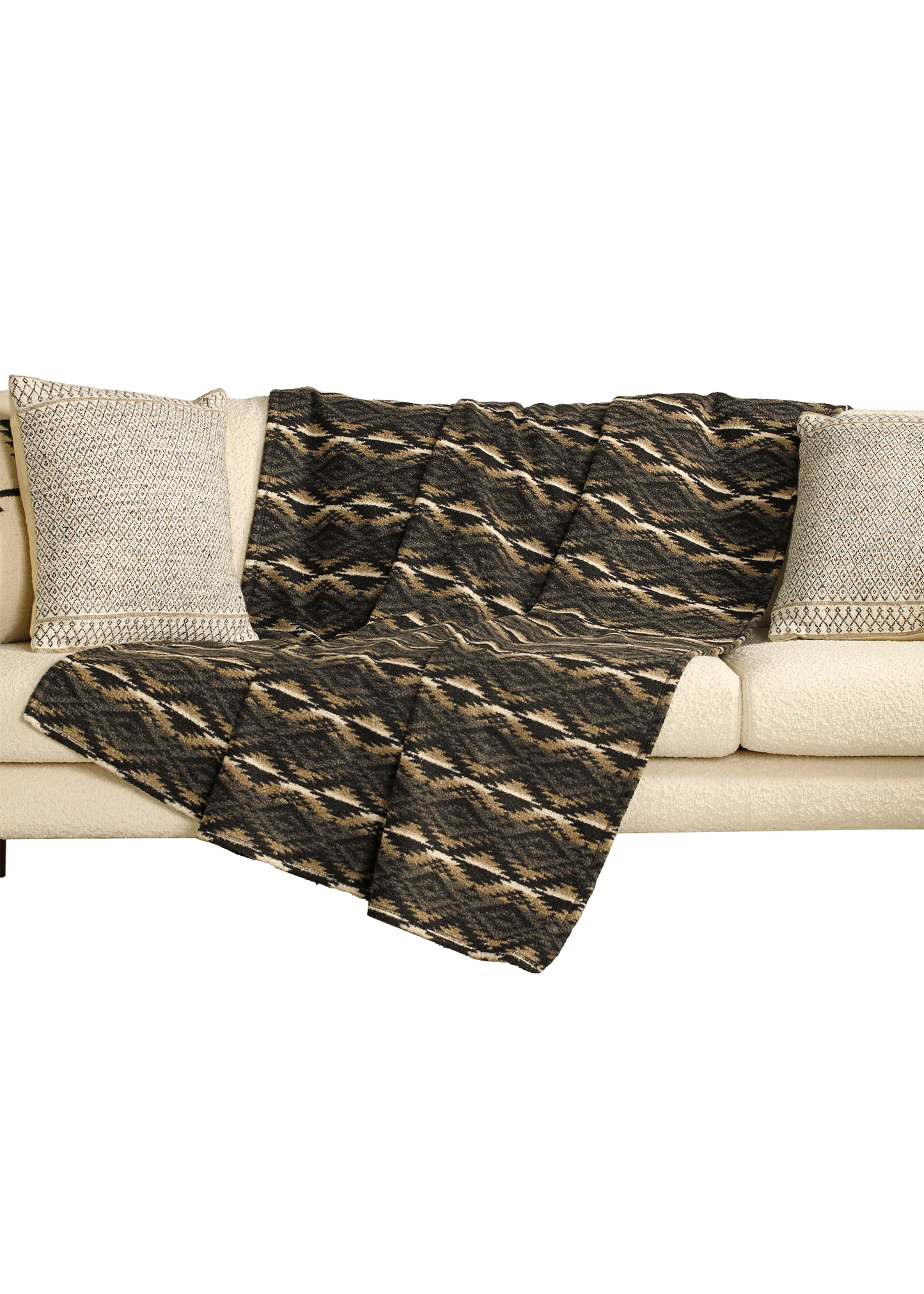 Patterned throw blanket draped over a beige sofa with textured pillows on a white background