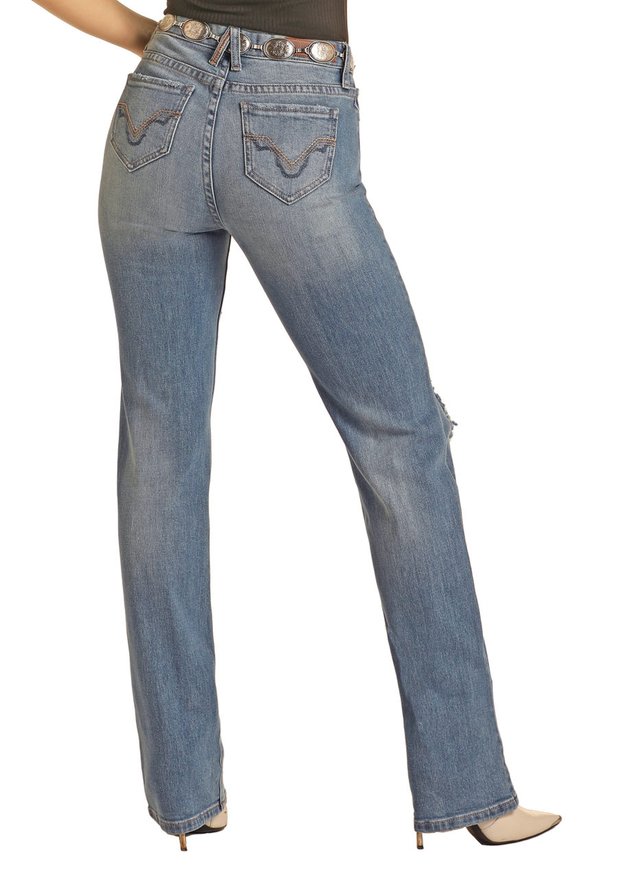 Someone is shown from the back against a white background, wearing Rock & Roll Denim’s West Desperado Distressed Denim High Rise Bootcut Jeans in light blue, paired with a black top, concho belt, and pointed-toe heeled shoes.