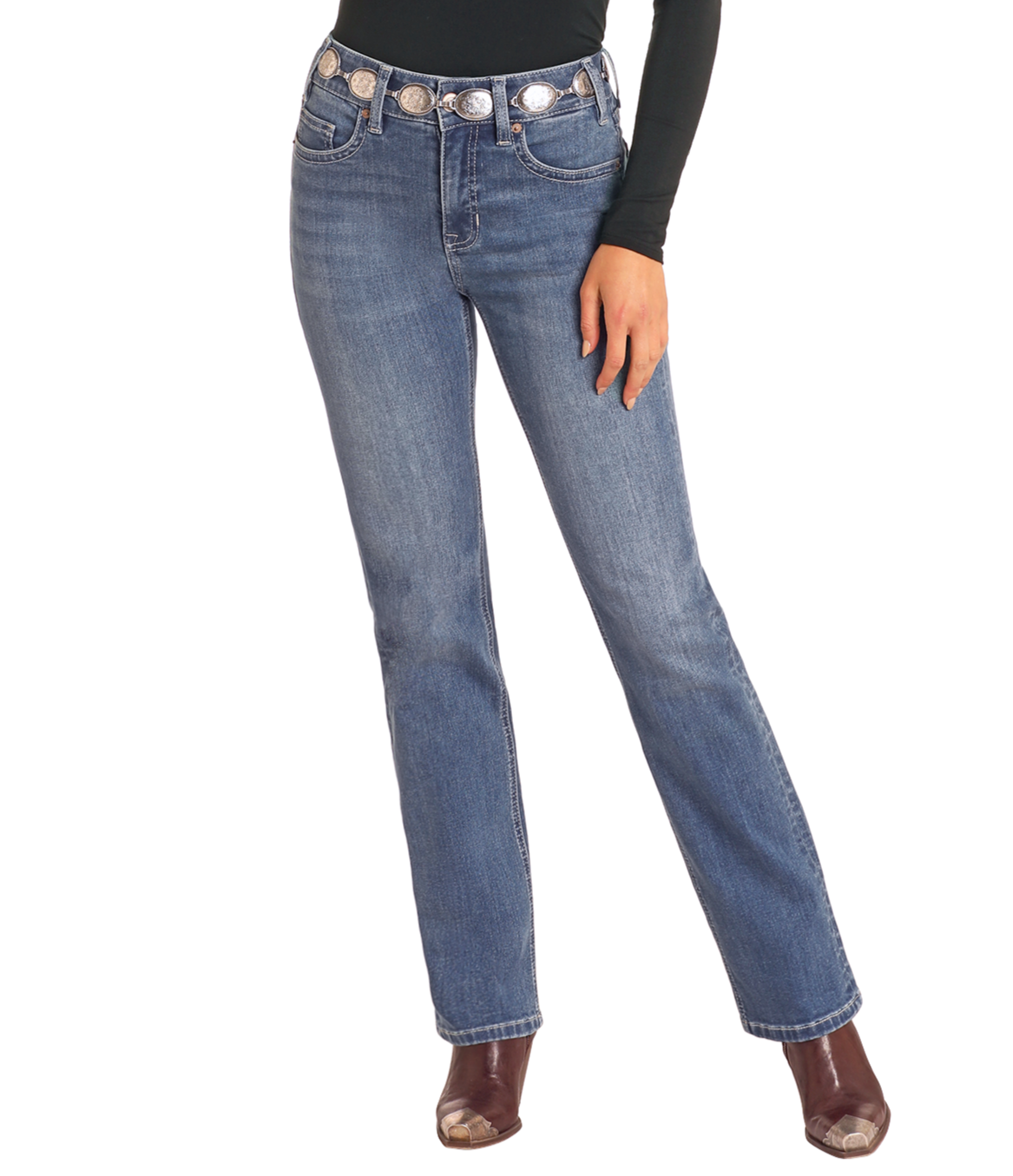 A person wearing Rock & Roll Denim High Rise Bootstitch Modest Bootcut Jeans in Medium Wash (30x34), a black long-sleeve top, silver concho belt, and brown heeled boots stands against a light background.