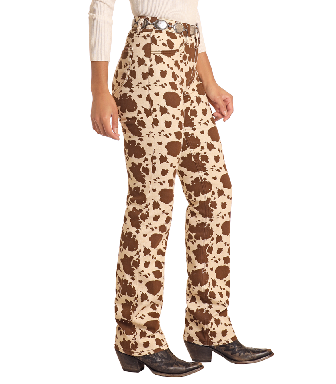 A person wears Rock & Roll Denim Cowhide Print Modest Bootcut Jeans, a tan belt, black cowboy boots, and a light long-sleeve top, standing against a white background.