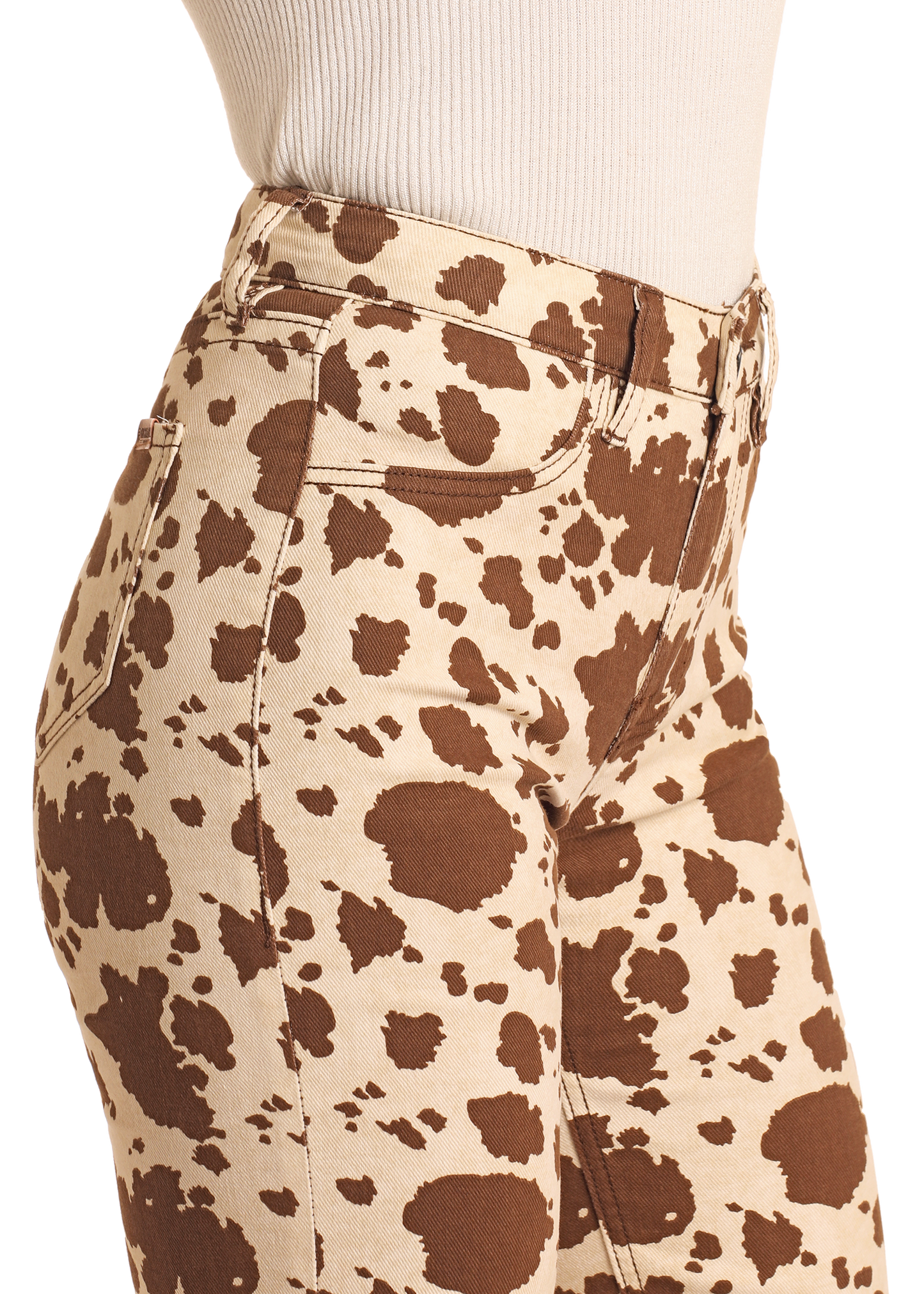 A person wearing Rock & Roll Denim Cowhide Print Modest Bootcut Jeans, featuring a brown and beige cow print pattern, paired with a light beige ribbed top; shown from waist to mid-thigh in a side profile.