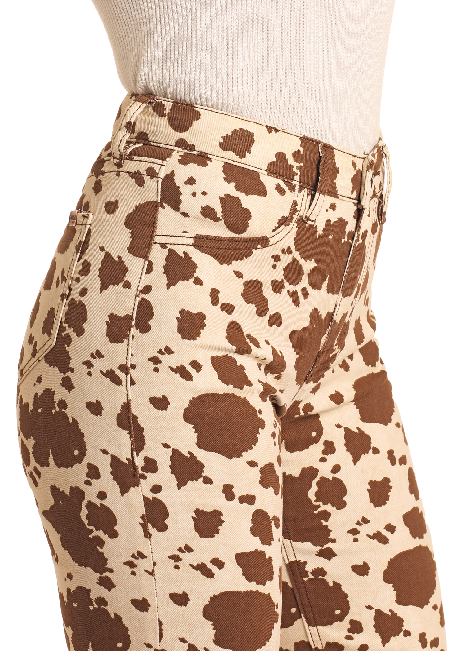 A person wearing Rock & Roll Denim Cowhide Print Modest Bootcut Jeans, featuring a brown and beige cow print pattern, paired with a light beige ribbed top; shown from waist to mid-thigh in a side profile.