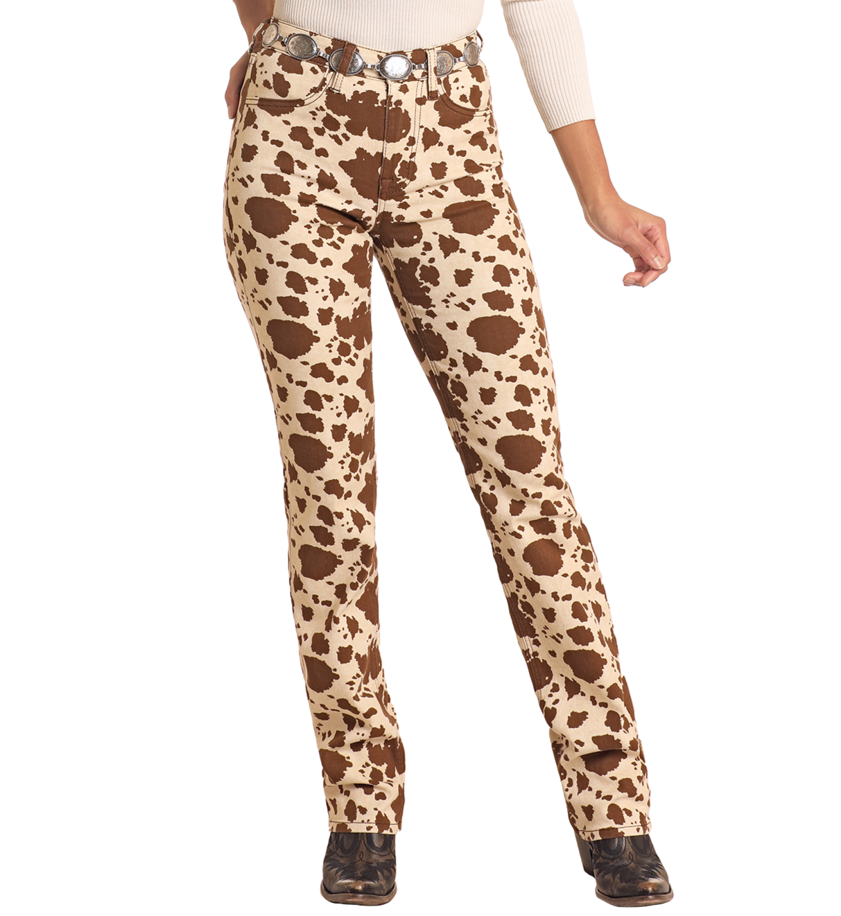 A person in Rock & Roll Denim Cowhide Print Modest Bootcut Jeans, a white long-sleeve top, silver concho belt, and black shoes stands against a plain white background.