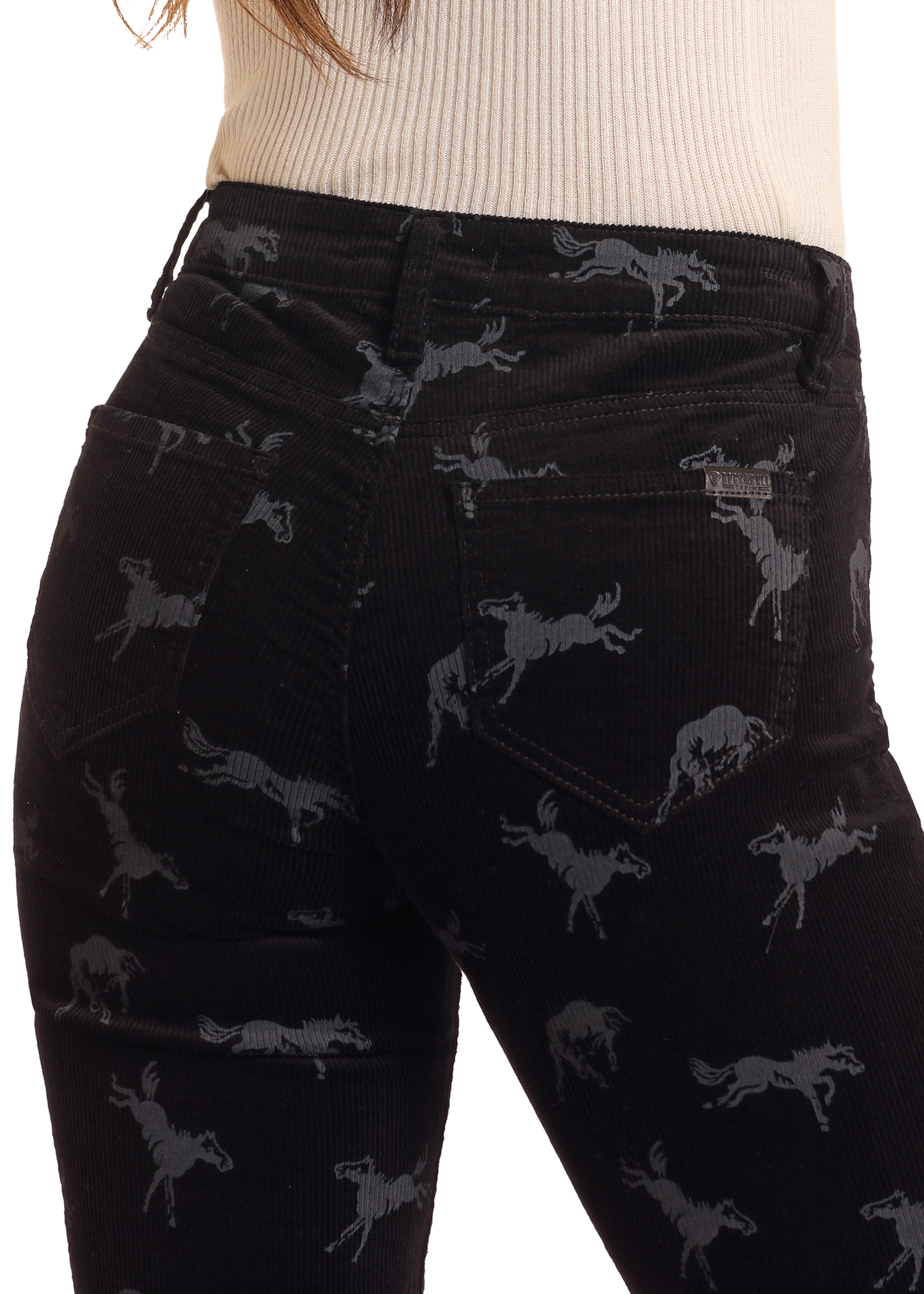 A person modeling Rock & Roll Denim's Corduroy Horse Print Modest Bootcut Jeans, featuring black fabric with a gray horse print, shown from the waist down paired with a beige ribbed top, offers a stylish yet modest high-rise look.