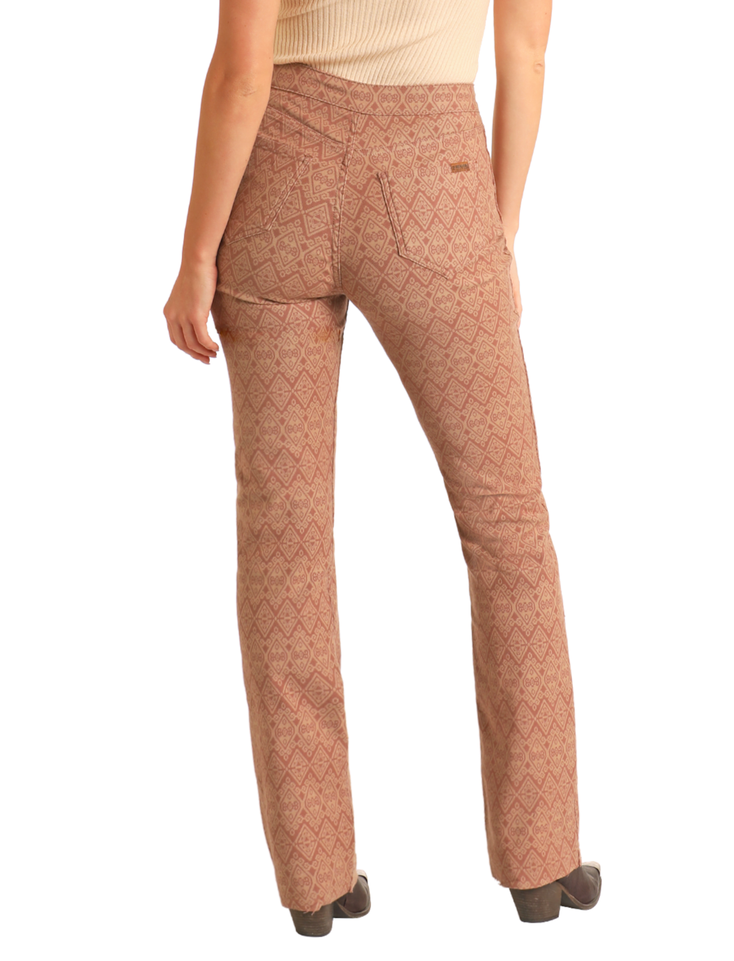 A person faces away from the camera wearing Rock & Roll Denim Reversible Aztec Modest Bootcut Jeans with a zigzag design, paired with a beige sleeveless top, brown patterned pants detail, and heeled shoes to complete the outfit.