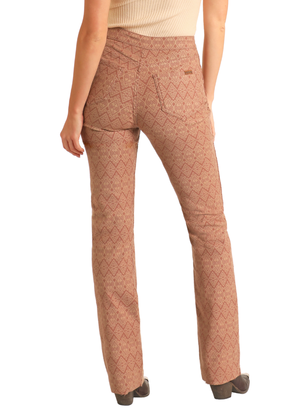 A person faces away from the camera wearing Rock & Roll Denim Reversible Aztec Modest Bootcut Jeans with a zigzag design, paired with a beige sleeveless top, brown patterned pants detail, and heeled shoes to complete the outfit.