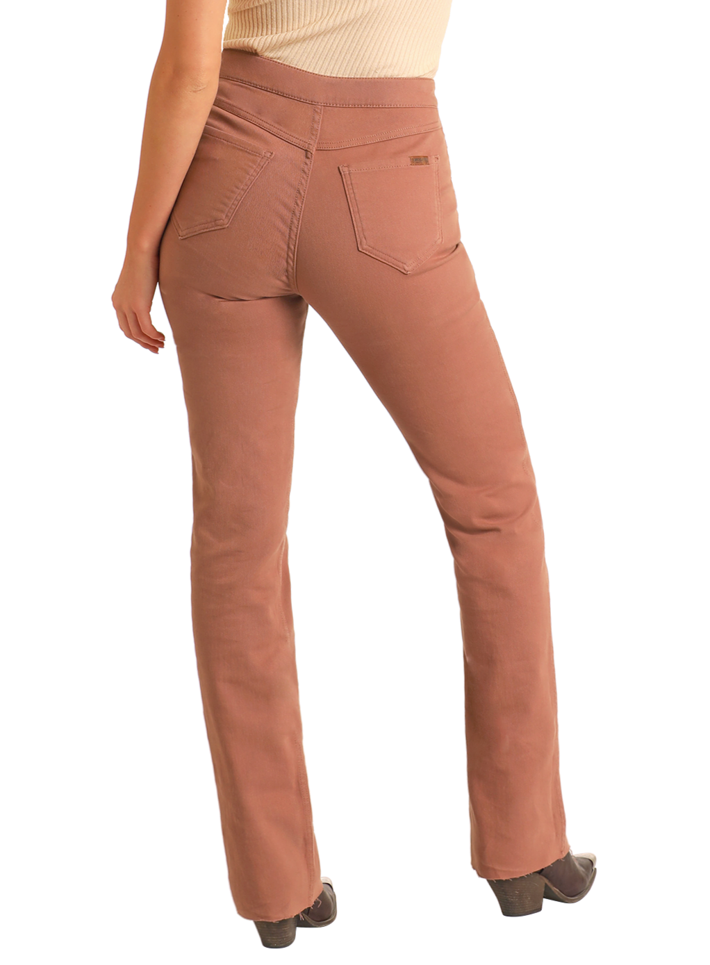 A person wearing high-waisted, dusty rose Reversible Aztec Modest Bootcut Jeans by Rock & Roll Denim and dark shoes is seen from the back. The jeans have two back pockets, a slim bootcut fit, and are paired with a beige top.