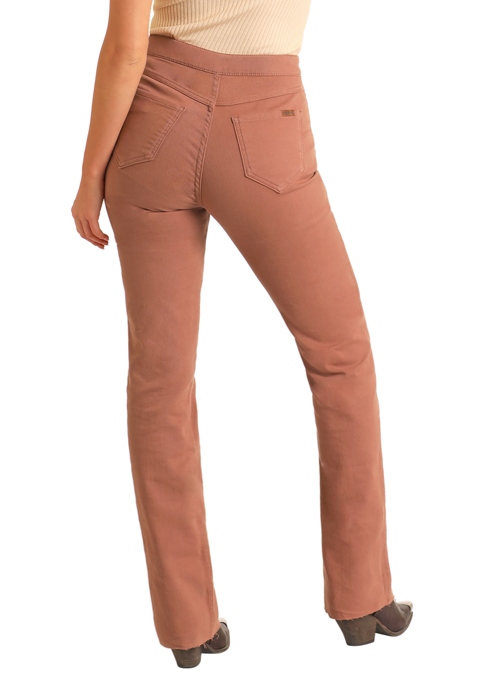 A person wearing high-waisted, dusty rose Reversible Aztec Modest Bootcut Jeans by Rock & Roll Denim and dark shoes is seen from the back. The jeans have two back pockets, a slim bootcut fit, and are paired with a beige top.