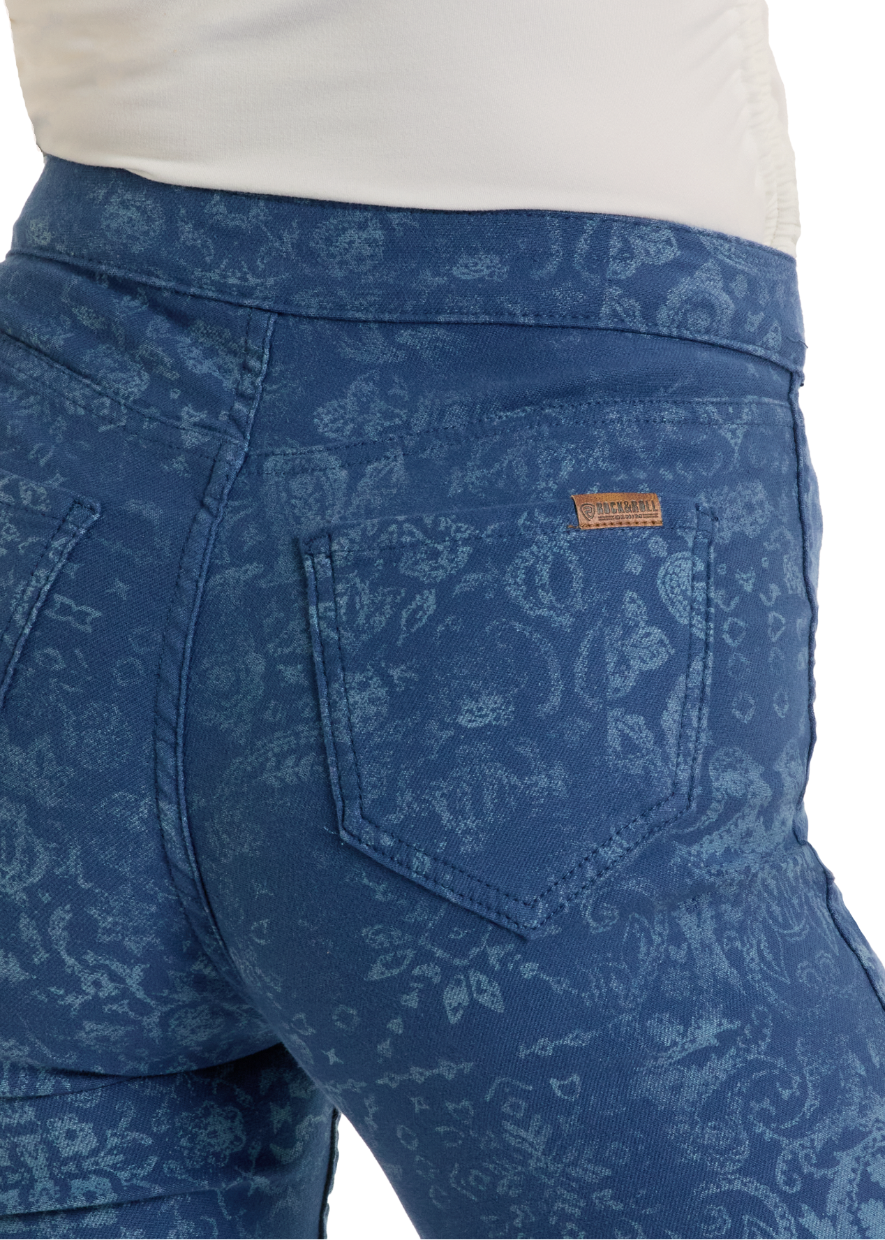 Close-up of a person in Rock & Roll Denim Reversible Bandana Modest Bootcut Jeans, featuring a subtle floral pattern, visible back pockets with orange stitching, a brown brand label above the right pocket, and paired with a white top.