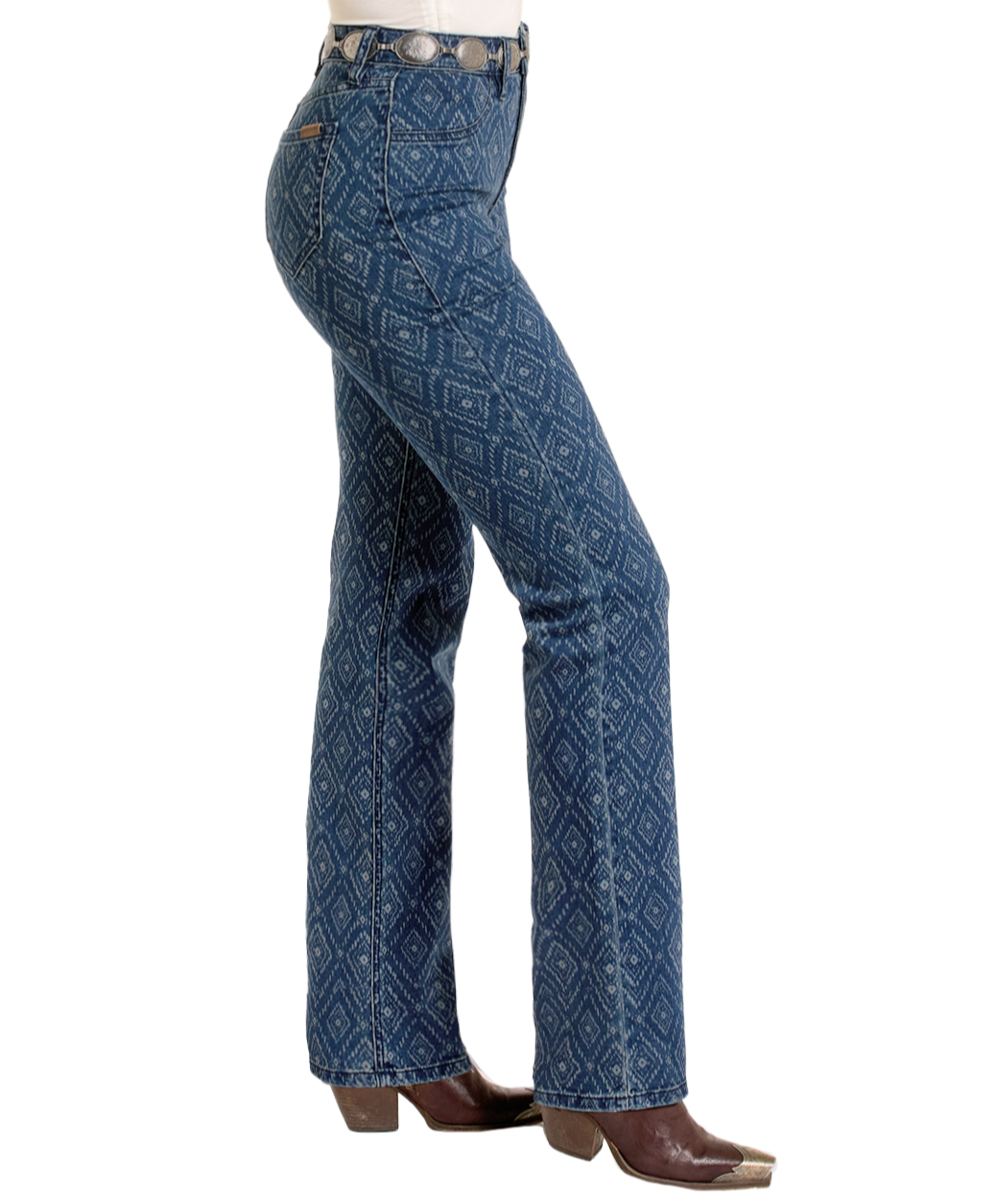 A person in Rock & Roll Denim High Rise Diamond Bootcut Jeans, a silver-buckled belt, and brown square-toed boots stands in profile against a plain white background.