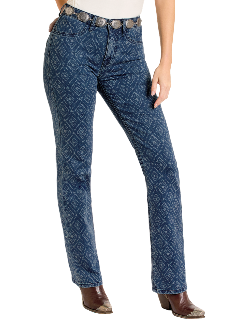A person wearing blue patterned Rock & Roll Denim High Rise Diamond Bootcut Jeans, a white shirt, a wide decorative belt, and brown pointed-toe boots stands with one hand resting on their thigh.