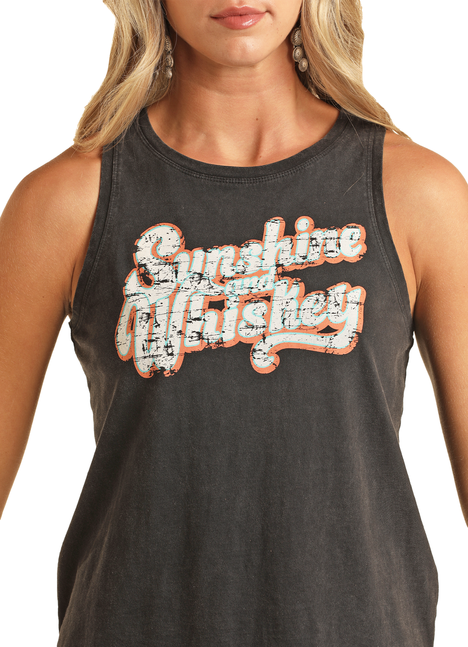 A woman models the Rock & Roll Denim Sunshine & Whiskey Graphic Tank Top, featuring distressed white and orange text. She accessorizes casually with earrings and stands against a plain white background with long blonde hair.