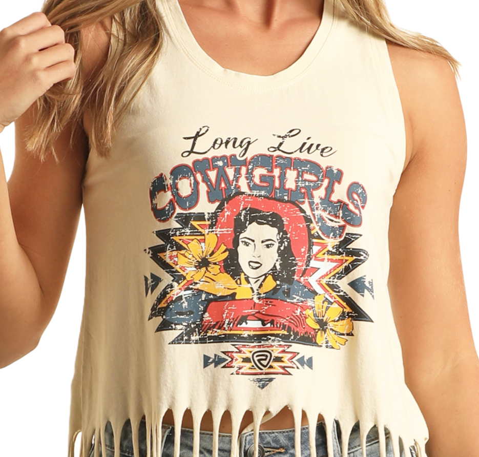 A woman wears the Rock & Roll Denim Cowgirl Graphic Fringe Tank Top, a sleeveless cream top with western flair, colorful cowgirl graphic, yellow flowers, and “Long Live Cowgirls” text.
