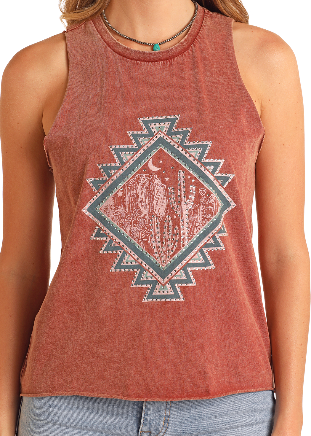 A person wears the Rock & Roll Denim Cactus Graphic Tank, a sleeveless, faded red mineral wash top featuring cacti, a crescent moon, and mountains inside a geometric diamond. They pair it with light blue jeans and a necklace.