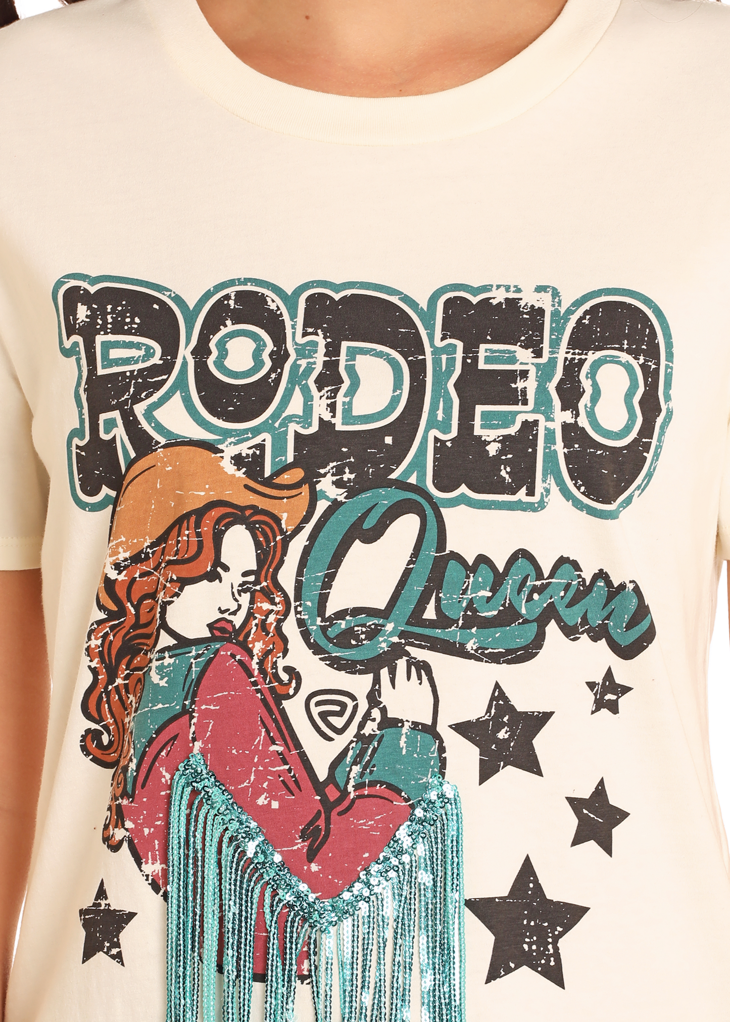 The Rodeo Queen Sequin Fringe Tee by Rock & Roll Denim features a cream color, sequin teal fringe, a vintage graphic of a red-haired cowgirl in a western hat, black stars, and distressed "RODEO Queen" text.
