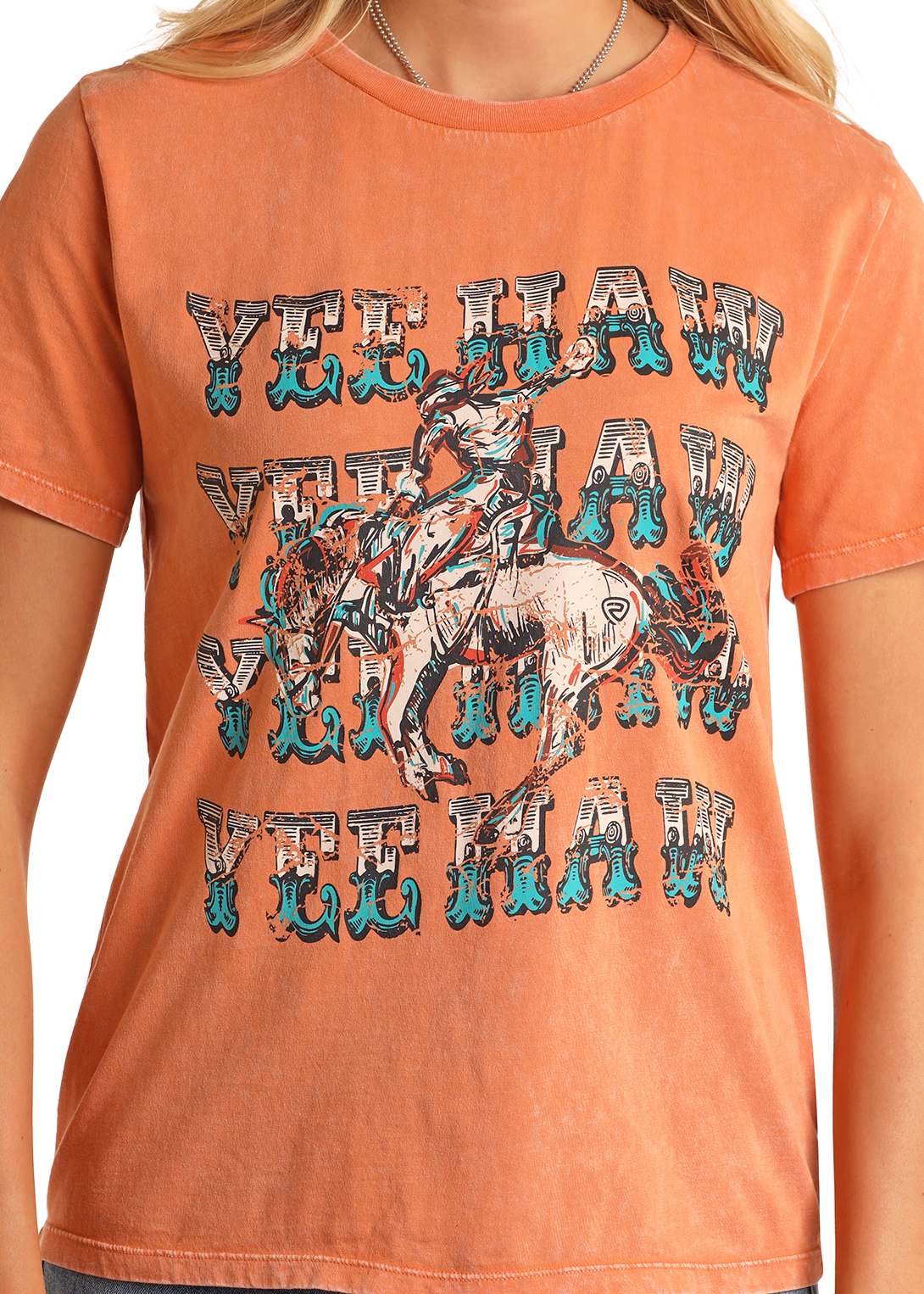 A person wears the Rock & Roll Denim Yeehaw Graphic Tee, made from 100% cotton, showcasing repeated YEE HAW text and a bold cowboy-on-bronc graphic on the front.