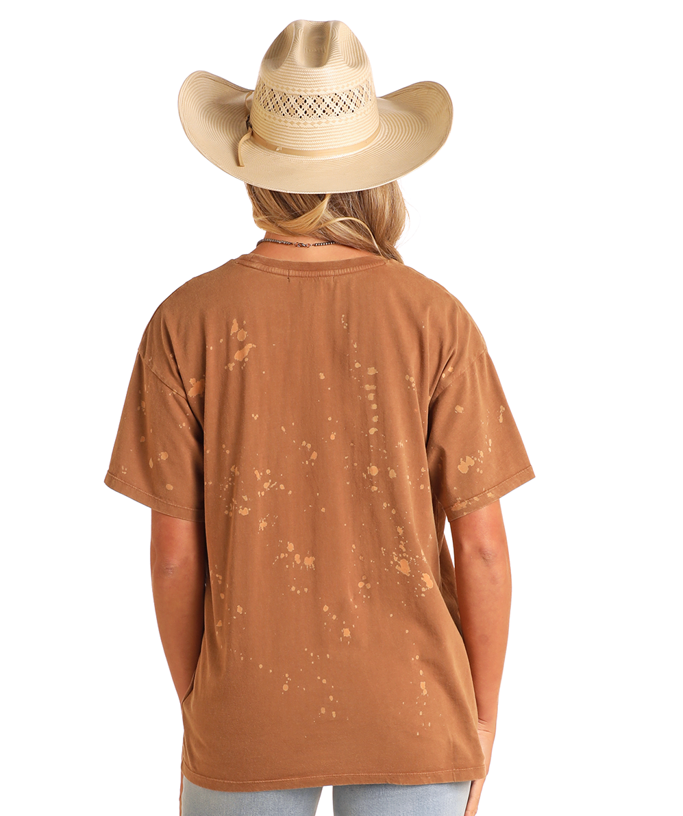 A person wearing a light tan cowboy hat and the Rock & Roll Denim Keep Her Wild Oversized Tee with a distressed Western graphic is seen from behind against a plain white background.