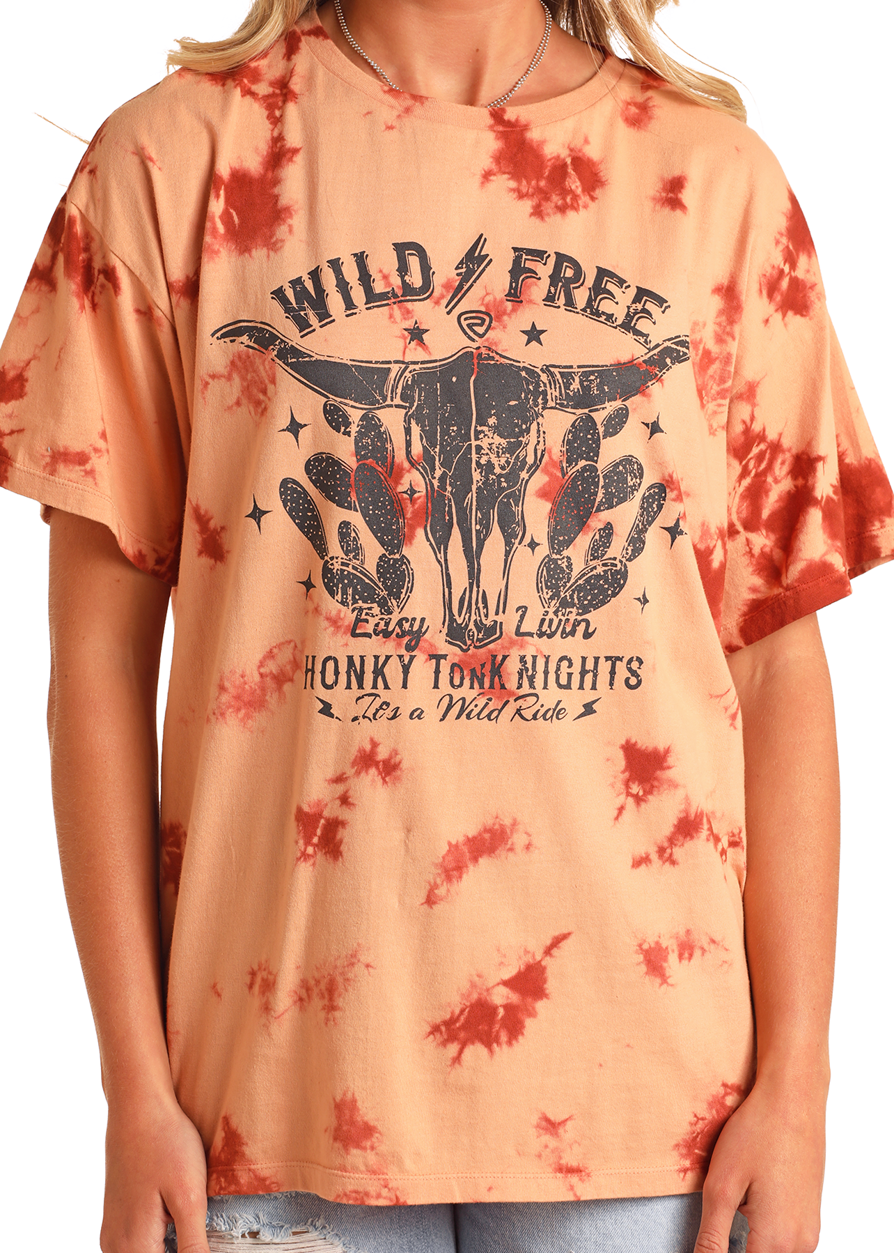Someone wears the Rock & Roll Denim Tie-Dye Oversized Tee, featuring a distressed bull skull Western graphic with bold phrases: WILD & FREE, Easy Livin, HONKY TONK NIGHTS, and It’s a Wild Ride in vibrant red and orange tones.