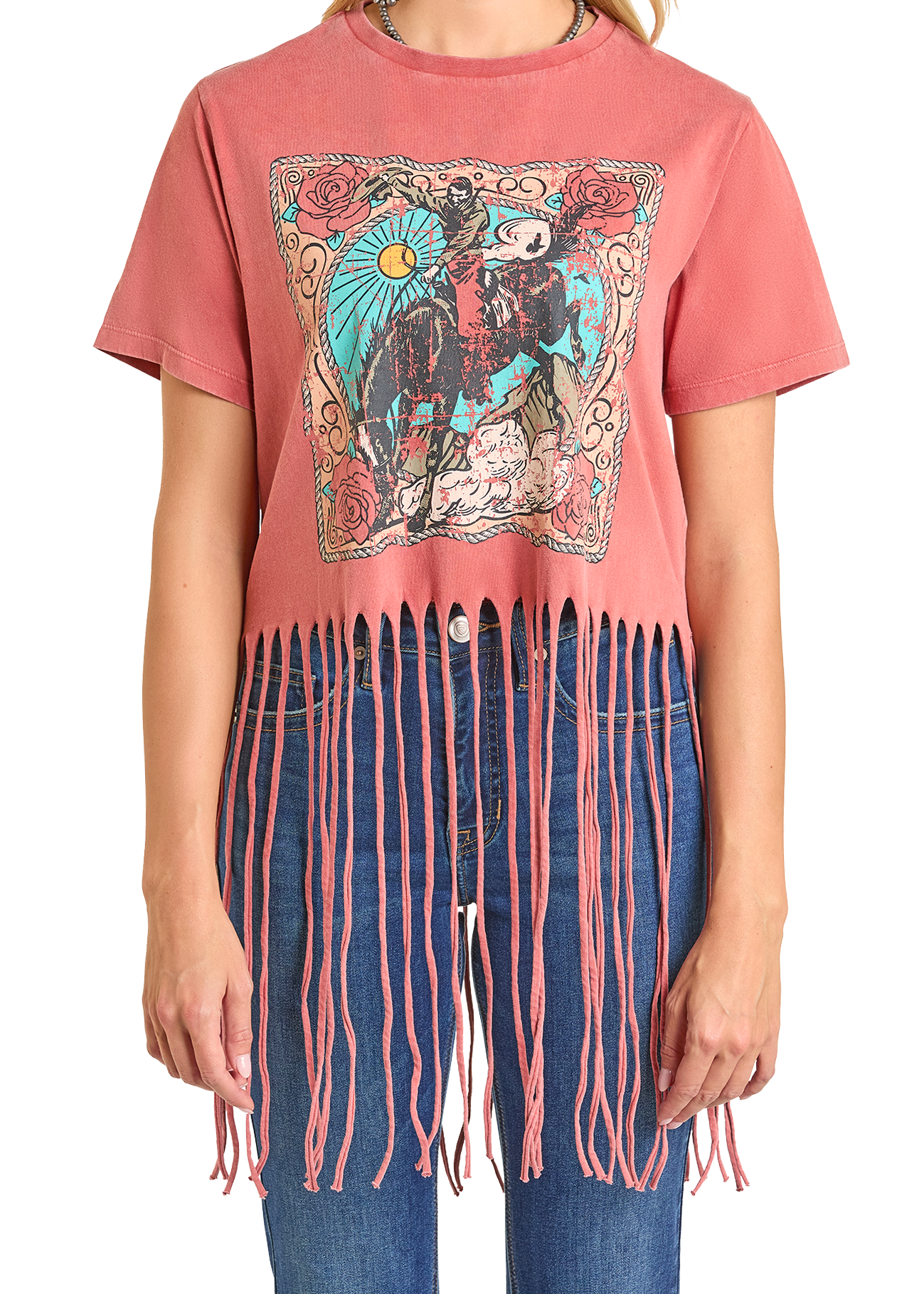 A person wears the Rock & Roll Denim Horse Graphic Fringe Tee, featuring a colorful cowboy and horse under the sun with long, pink knotted fringe at the hem, paired with blue jeans.