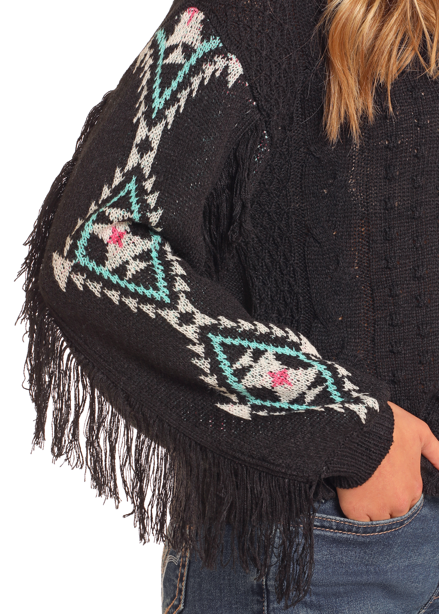 A person wears the Rock & Roll Denim Aztec Fringe Cable Knit Sweater in black with colorful geometric sleeve patterns and blue jeans. Only the torso and part of one arm are shown.