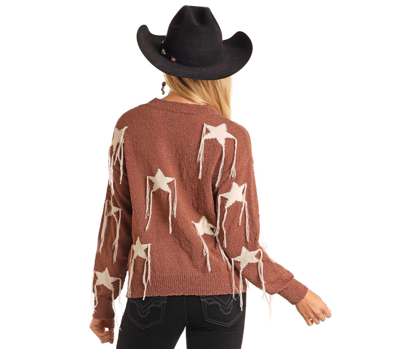 Someone wearing a black cowboy hat and the Rock & Roll Denim Star Fringe Sweater, featuring white stars and fringe details, stands with their back to the camera against a plain background.