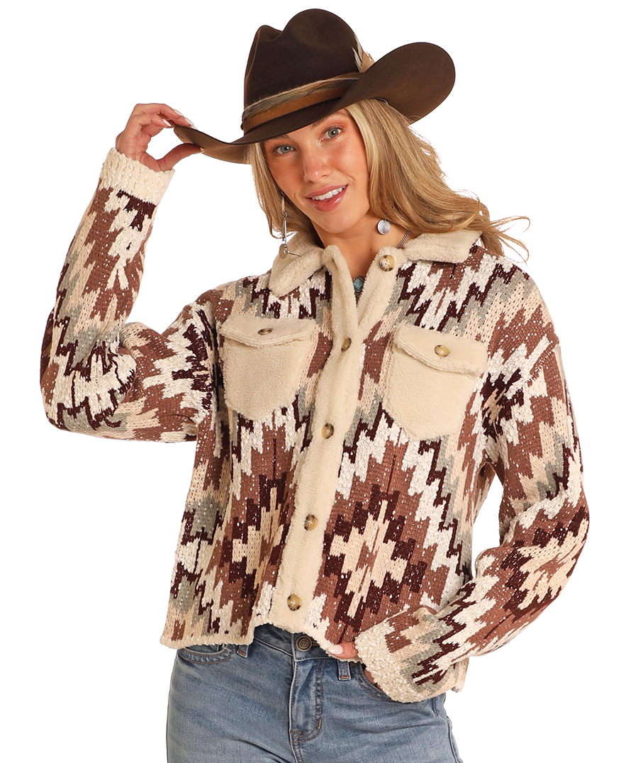 A woman smiles in a Rock & Roll Denim Aztec Button Up Sweater Cardigan with front pockets, wearing a cowboy hat and blue jeans, holding the brim of her hat with one hand.