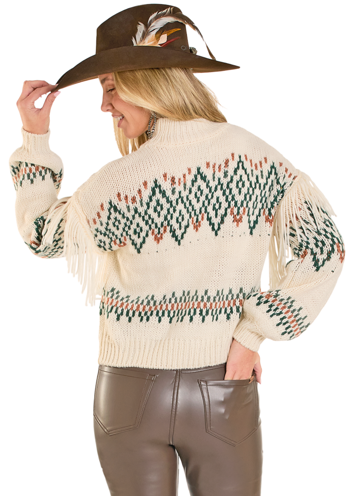 Woman wearing a cream-colored sweater with patterned design and fringes, holding a brown hat with feathers.