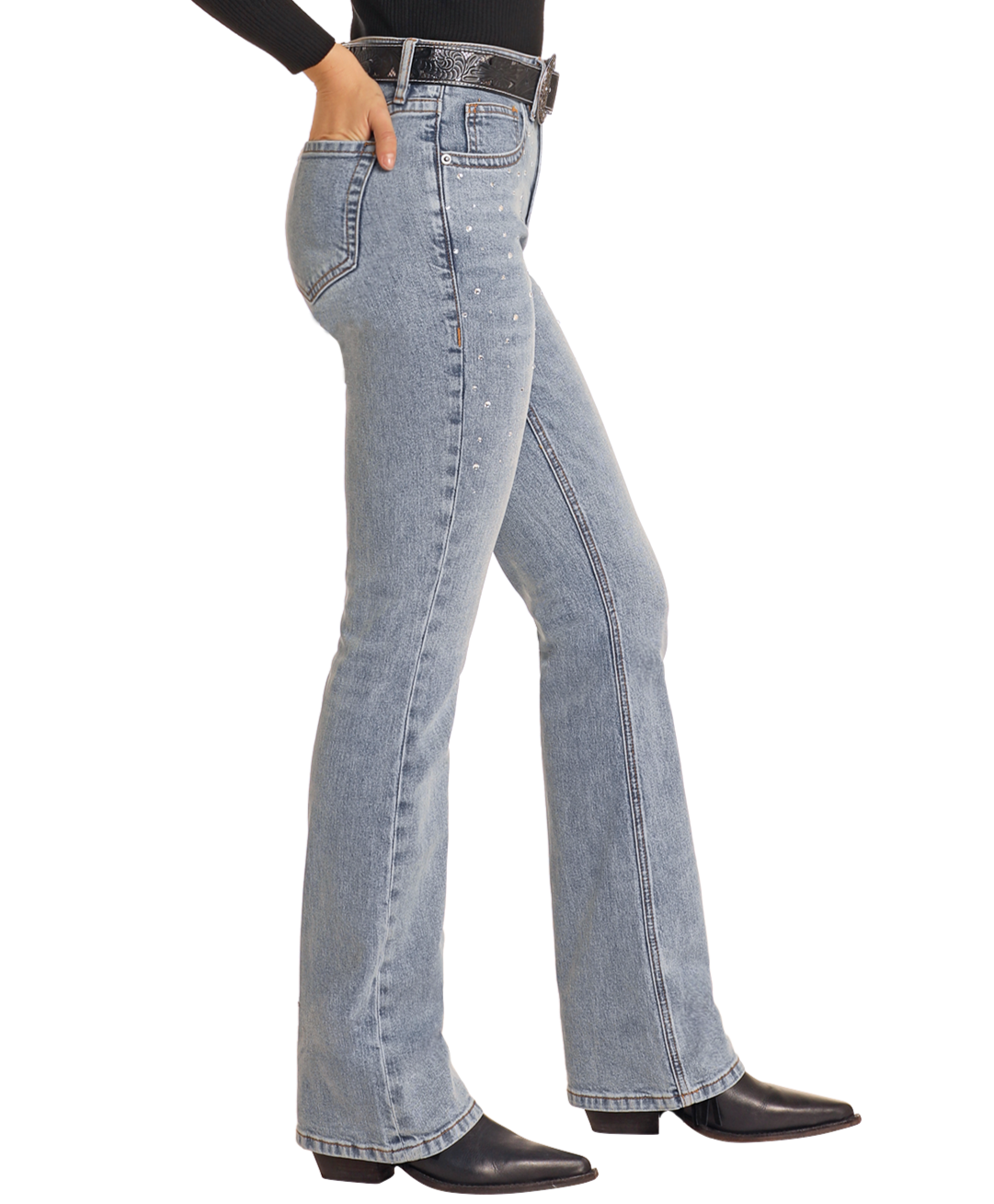 Wearing Rock & Roll Denim High Rise Diamond Studded Bootcut Jeans, a person stands in side profile with black heeled boots and a black belt against a plain white background.