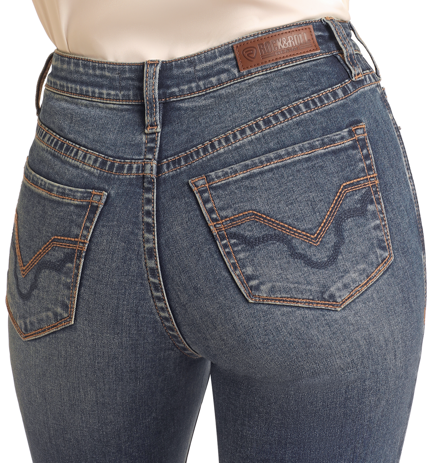 Model wearing Rock & Roll Denim Mid Rise Signature Bootcut Jeans in blue wash with brown stitching, two back pockets, and a leather patch on the waistband. Shown from the waist down and behind.