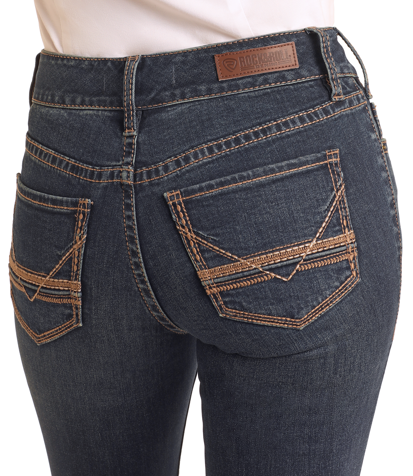 Close-up of a person wearing Rock & Roll Denim Mid Rise V Stitch Bootcut Riding Jeans, featuring contrast stitching, embroidered back pockets, and a brown leather patch with brand label on the waistband.
