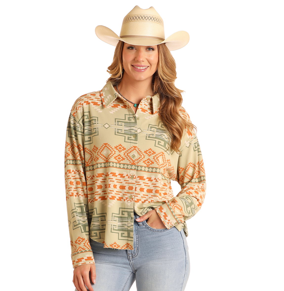 A woman in a green Rock & Roll Denim Aztec Knit Overshirt, tan cowboy hat, and light blue jeans smiles with one hand in her pocket.