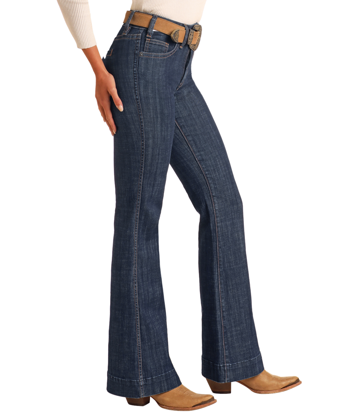 Someone stands against a plain light background wearing Rock & Roll Denim High Rise Welt Pocket Trouser Jeans in dark blue, paired with a tan belt, tan cowboy boots, and a cream long-sleeve top.