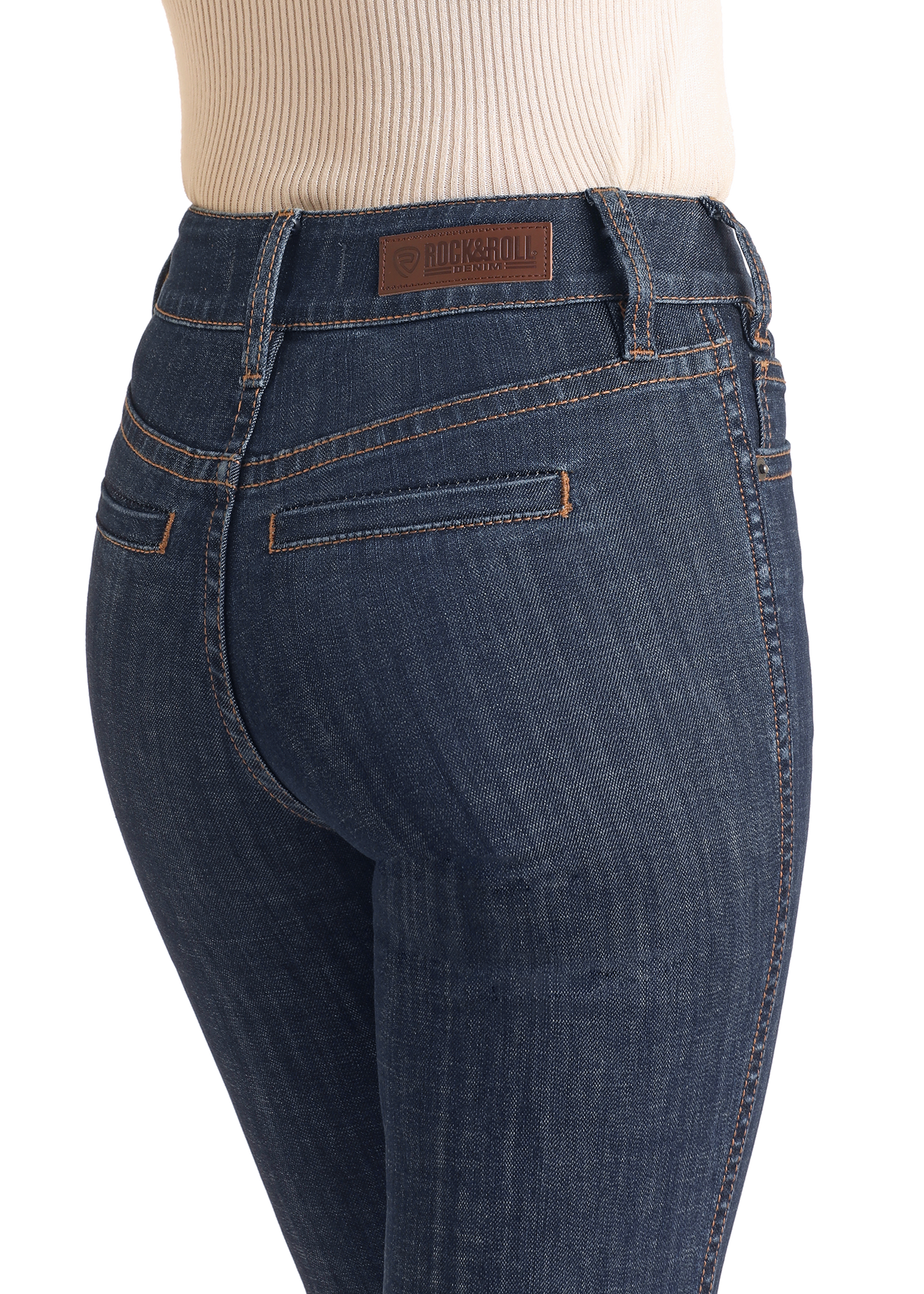 A person wears Rock & Roll Denim High Rise Welt Pocket Trouser Jeans with contrast stitching, a brown leather Rock & Roll patch on the waistband, and a tan ribbed top. The close-up image focuses on the waist and hips.