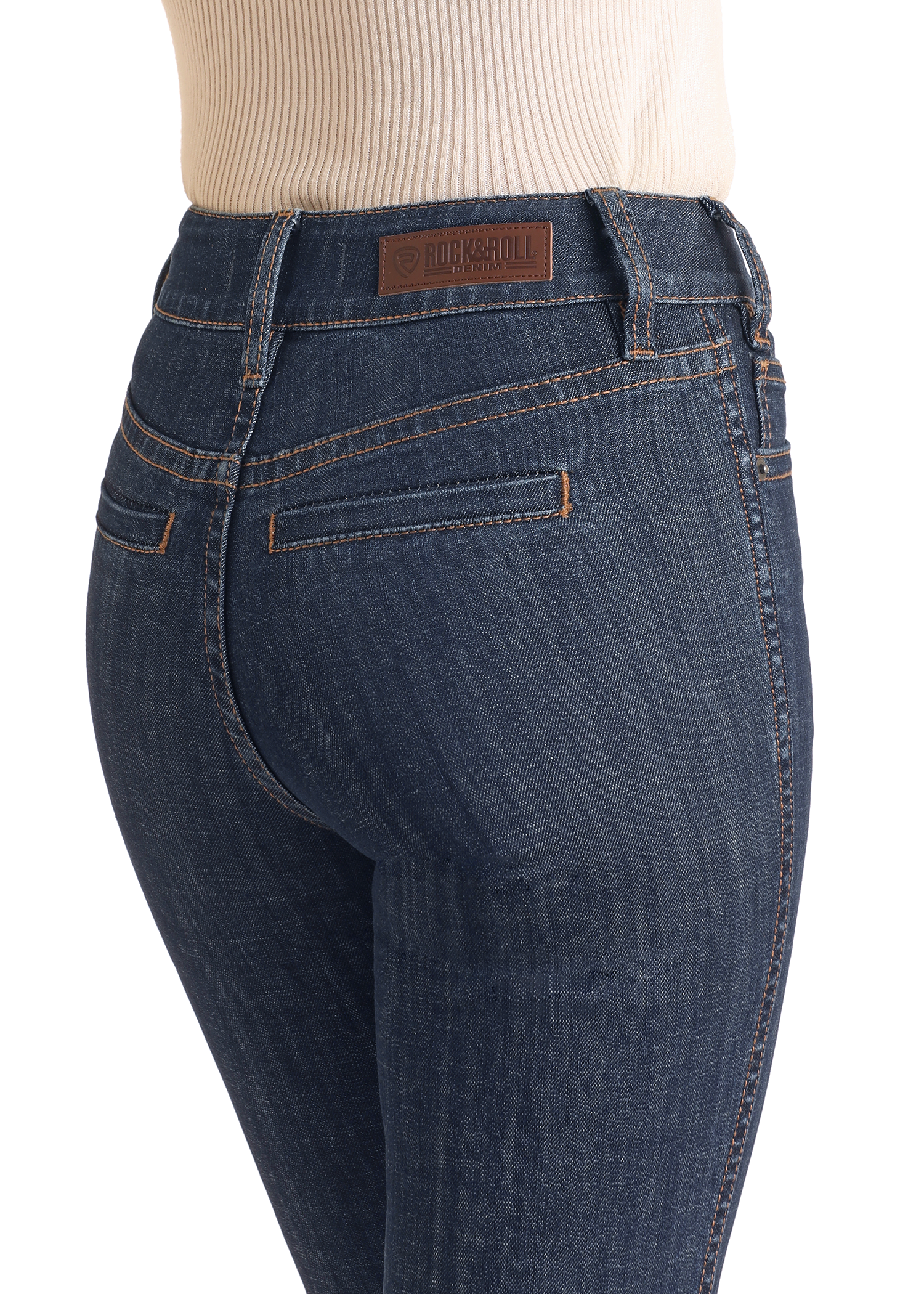 A person wears Rock & Roll Denim High Rise Welt Pocket Trouser Jeans with contrast stitching, a brown leather Rock & Roll patch on the waistband, and a tan ribbed top. The close-up image focuses on the waist and hips.
