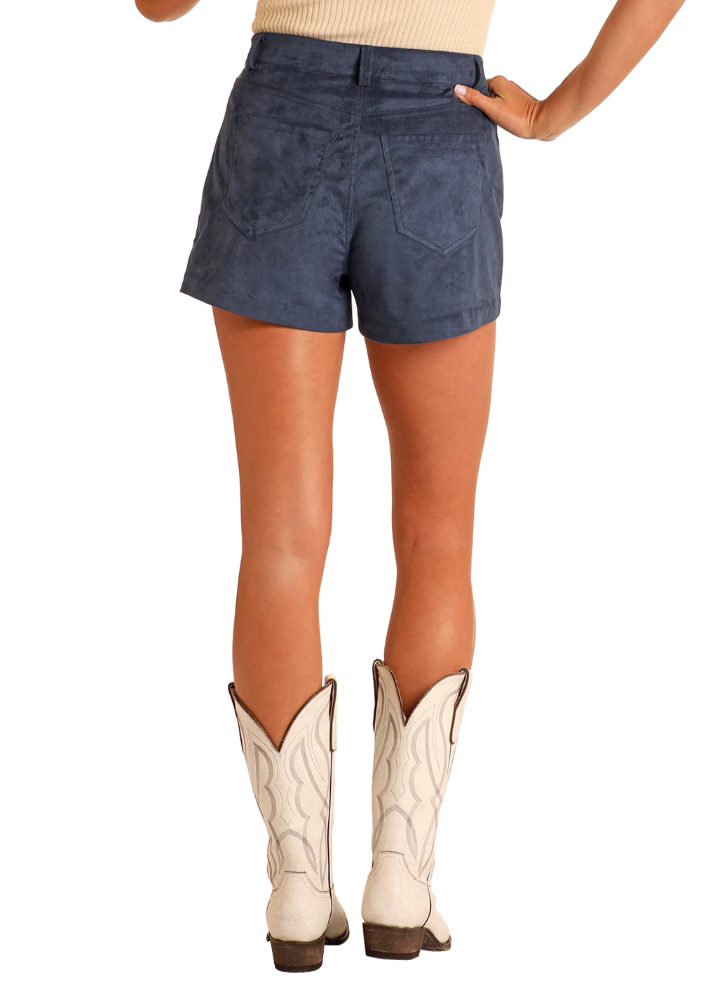 A person stands facing away, wearing Rock & Roll Denim’s Star Studded Microsuede Shorts, a beige sleeveless top, and white cowboy boots with decorative stitching.