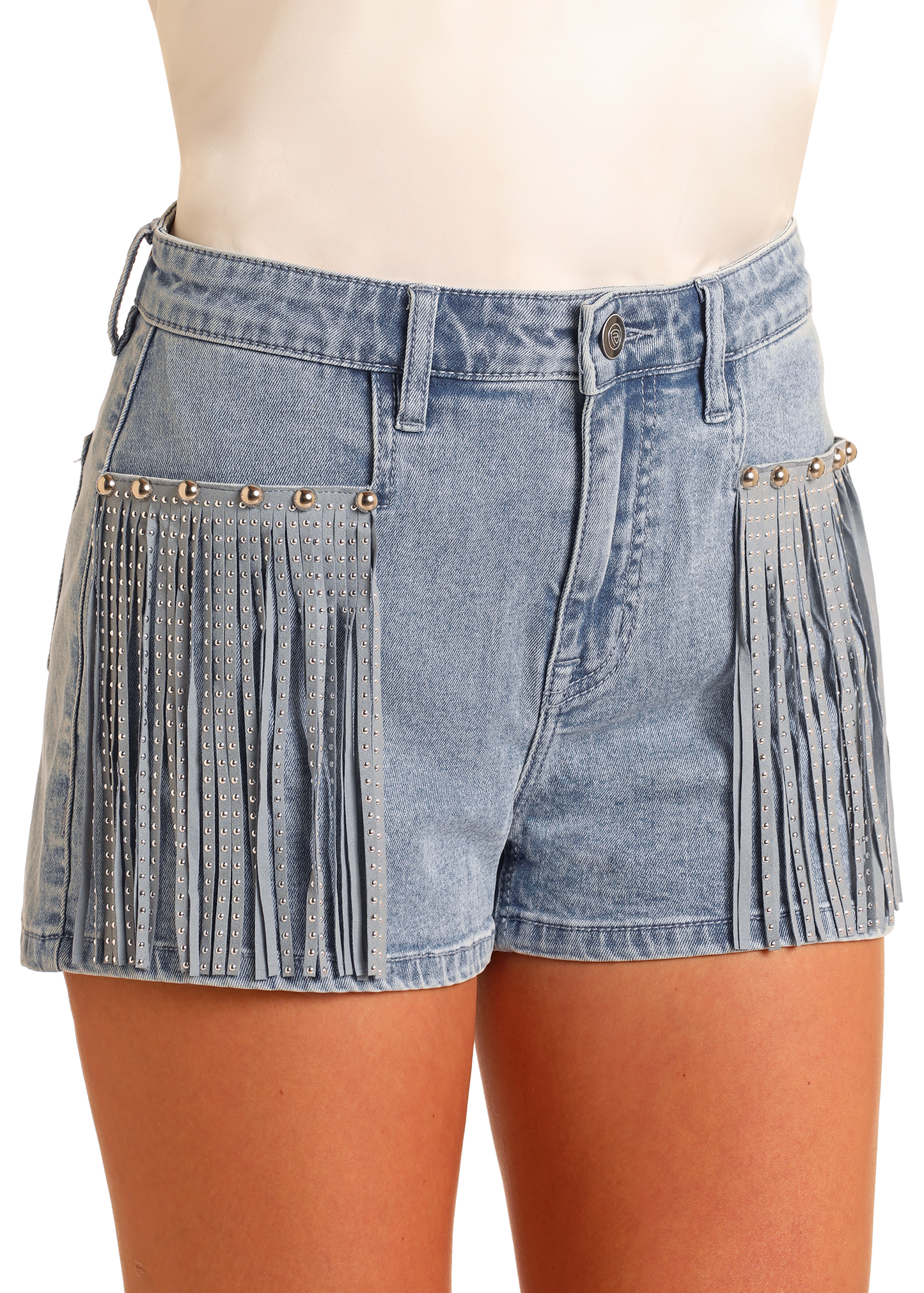 A woman models Rock & Roll Denim Extra Stretch Studded Fringe Shorts in light blue, featuring silver accents and a Western-inspired look. Paired with a white top, the photo highlights the shorts without revealing the model’s face.