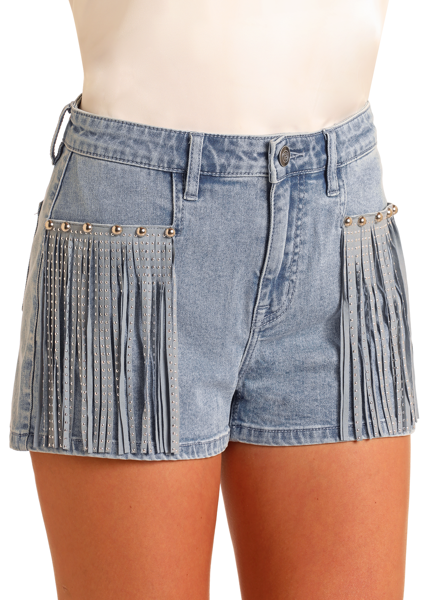 A woman models Rock & Roll Denim Extra Stretch Studded Fringe Shorts in light blue, featuring silver accents and a Western-inspired look. Paired with a white top, the photo highlights the shorts without revealing the model’s face.