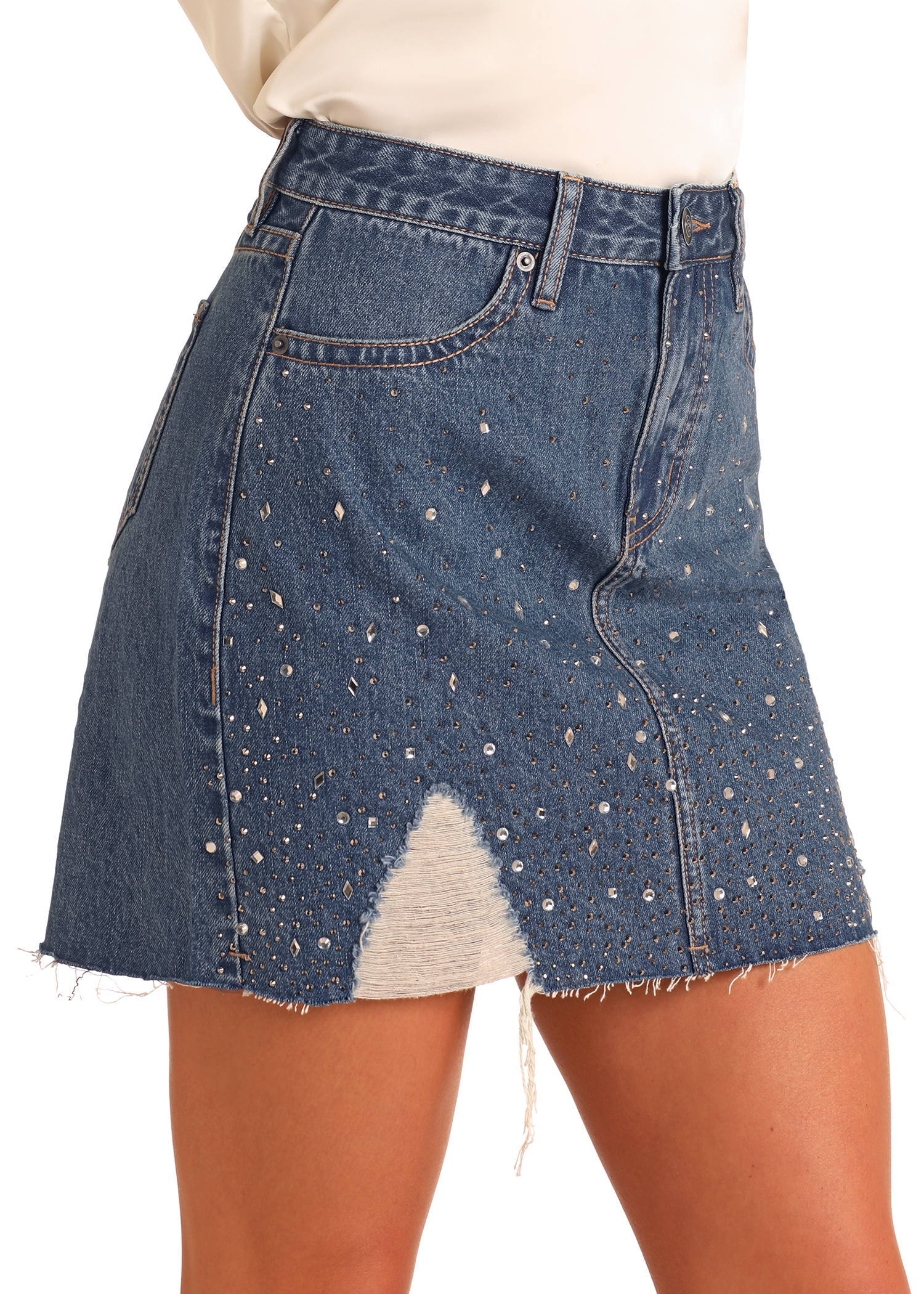 A woman wears the Rock & Roll Denim Distressed Studded Denim Mini Skirt, featuring a high-rise fit, frayed hem, silver studs, and a triangular distressed patch on the front.