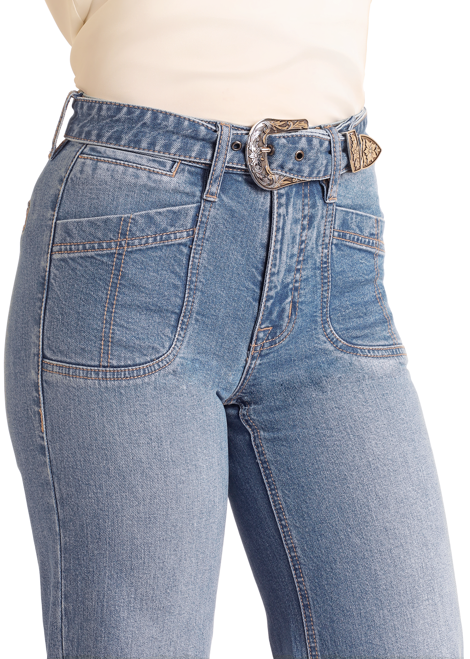 A close-up of a person wearing Rock & Roll Denim High Rise Belted Relaxed Flare Jeans with front pockets, paired with a cream top and a decorative denim Western belt with an engraved silver buckle.