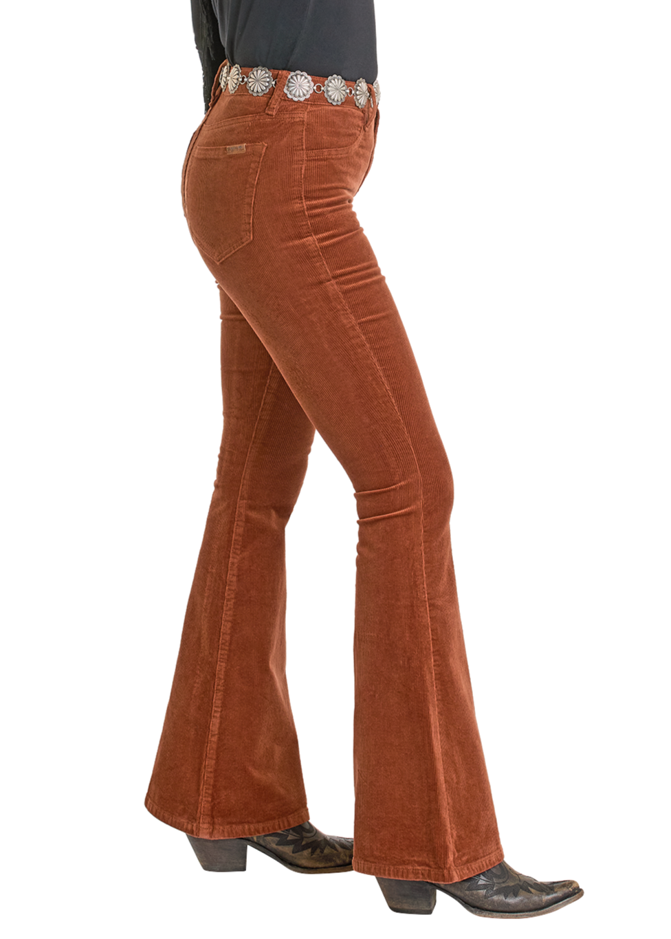 A person is shown from the side against a white background wearing Rock & Roll Denim Rust Corduroy Flare Jeans with a black belt featuring large silver conchos and black heeled boots.