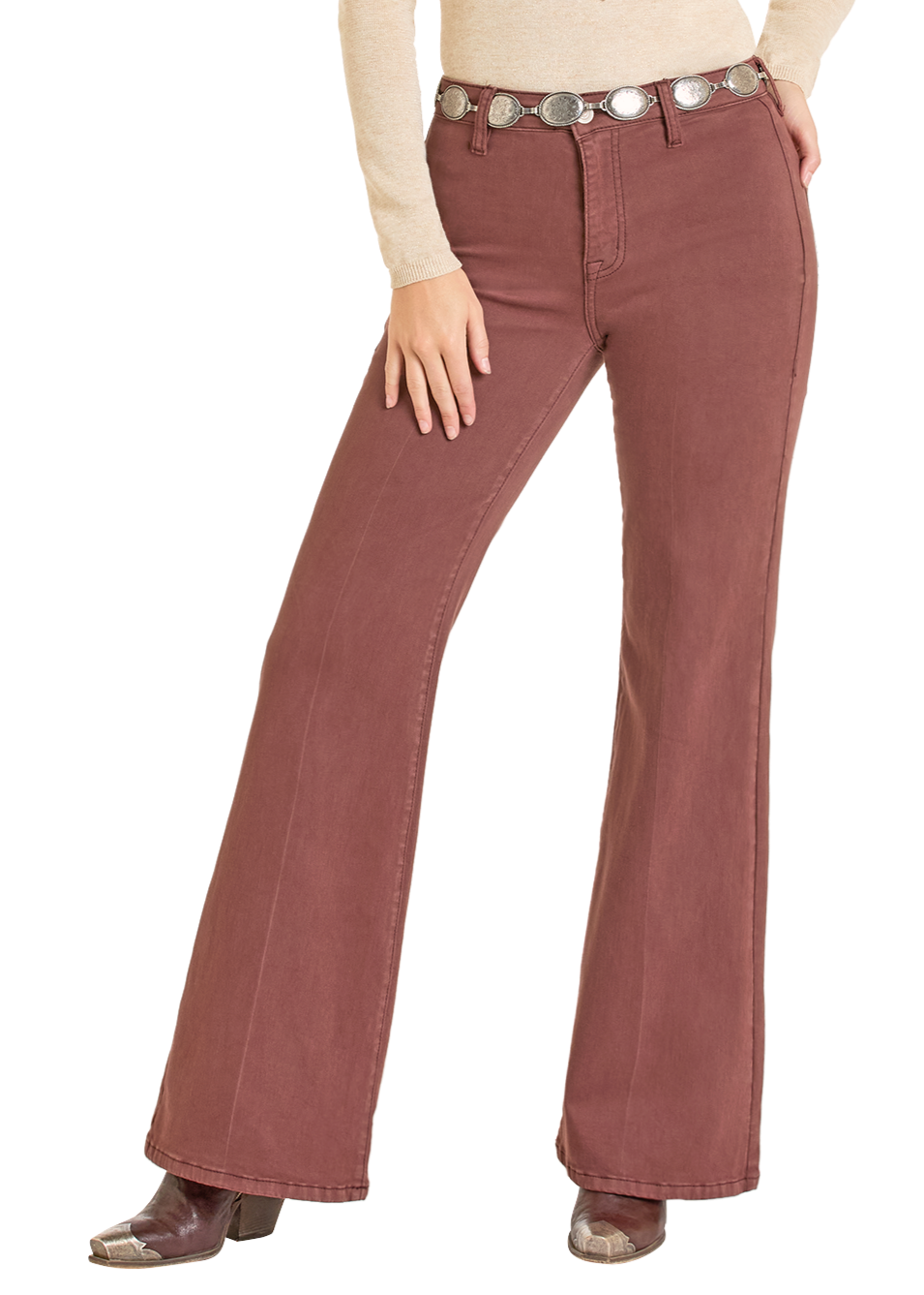 A person stands with one hand on their hip, wearing Rock & Roll Denim High Rise Wine Button Flare Jeans, a beige long-sleeve top, a silver concho belt, and brown snakeskin boots.
