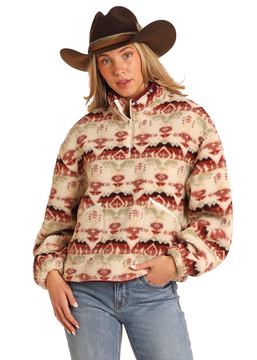 A person in a brown cowboy hat and the Rock & Roll Denim Aztec Print Sherpa Pullover with red and beige designs, paired with blue jeans, stands with one hand in their pocket against a plain background.